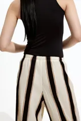 Pantalón de punto color crema con rayas verticales negras y marrones, de corte holgado y tiro alto, con cintura elástica y cordón ajustable.