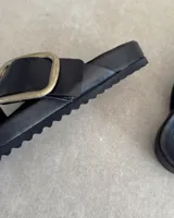 Sandalias negras de cuero con dos tiras anchas cruzadas y hebilla metálica dorada.