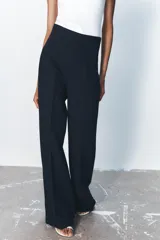 Pantalón negro de tiro alto y corte acampanado, con cierre frontal de cremallera dorada.