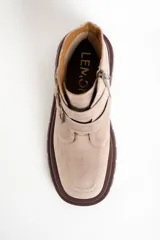 Bota corta de cuero color rosa viejo o beige claro, con suela track gruesa color marrón oscuro. Presenta dos tiras ajustables con hebillas metálicas color bronce y cierre lateral.