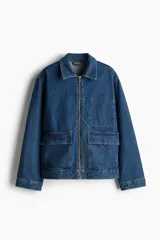 Campera de denim azul con cuello, cierre frontal y canesú en la espalda. Tiene puños abotonados, bolsillos delanteros con solapa y bolsillo interior de parche en el pecho.