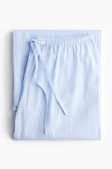Pantalón de pijama de corte holgado en algodón a rayas celestes y blancas. Modelo de tiro bajo con elástico revestido en la cintura, cordón para ajustar fino y piernas rectas, levemente acampanadas.
