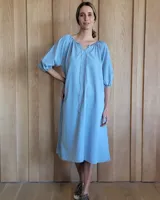 Vestido celeste de denim, corte amplio, con escote redondo con lazo ajustable, mangas 3/4 abullonadas con puños elásticos y largo midi.