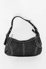 Cartera negra de denim con costuras blancas en contraste, cierre superior con cremallera y asa corta con hebilla ajustable.
