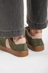 Zapatilla deportiva de cuero color verde oliva con detalles en rosa y suela marrón.