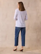 Blusa blanca de poliéster y rayón con escote en V bordado y mangas tres cuartos regulables con presilla y botón.