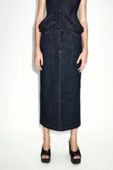 Falda midi de tiro alto confeccionada en denim oscuro, con cinco bolsillos estilo jean, cierre frontal con cremallera y botón, y abertura en la espalda. Presenta pespuntes en color rojo contrastante.