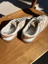 Championes de cuero color beige y blanco, con tachas plateadas en los laterales y suela de goma color caramelo.