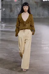 Blusa color marrón con escote en pico, manga larga abullonada con elástico en los puños y volantes en el escote y mangas.