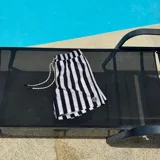 Short de baño negro con rayas verticales blancas, cintura elástica con cordón ajustable y logo de la marca en la pierna derecha.