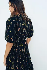 Vestido largo de algodón negro con estampado de flores pequeñas en tonos rosa y amarillo. Tiene cuello mao, mangas globo cortas, cinturón fino extraíble y falda acampanada con fruncido escalonado.