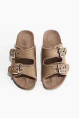 Sandalias planas color beige de gamuza sintética, con dos tiras anchas ajustables mediante hebillas metálicas plateadas.