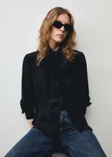 Blusa negra de tejido satinado con lazo al cuello, manga larga abotonada y cierre oculto de botones.