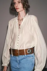 Camisa color crema de algodón con cuello redondo, escote pico con lazadas, manga larga con puños y cierre frontal con botones.