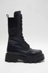 Bota de piel negra con suela dentada de goma y cierre de cremallera lateral, cordones frontales y puntera cuadrada.