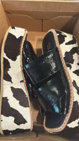 Sandalias de plataforma con suela de yute y capellada de cuero con estampado de vaca (blanco y negro). La capellada es de tiras cruzadas de charol negro brillante.