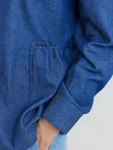 Camisa celeste de algodón con cuello clásico, cierre frontal con botones y mangas largas. Presenta volados en el frente y corte evasé.