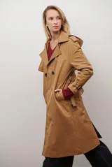 Trench coat largo color beige con doble botonadura, cuello solapa, cinturón ajustable y puños con tiras.