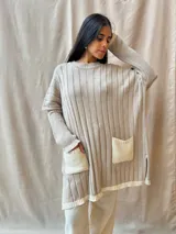 Sweater tejido de punto color beige, de corte holgado, con cuello redondo, mangas largas y bolsillos frontales.