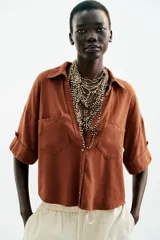 Camisa de lino color celeste claro, con cuello solapa, escote pico, manga corta con vuelta y dos bolsillos de plastrón en el delantero. Cierre frontal con botones.