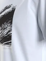 Remera blanca de algodón con cuello redondo y mangas cortas. Estampado rectangular en el frente con diseño abstracto en blanco y negro. Logo de Calvin Klein en el pecho y en la parte inferior del estampado.