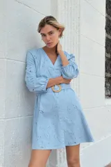 Vestido corto celeste con bordados calados, escote en V, mangas 3/4 abullonadas con elástico y cinturón con hebilla redonda de madera. Cierre frontal con botones.