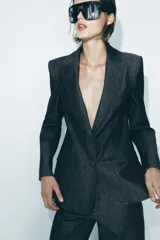 Blazer gris oscuro con cuello solapa, manga larga, bolsillos con solapa en el delantero y cierre frontal con dos botones forrados.