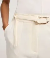 Pantalón de vestir color crudo, de corte recto, con bolsillos laterales y traseros. Se ajusta a la cintura con cinturón de cuero marrón con hebilla dorada.