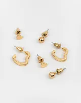 Set de tres pares de aros dorados: un par de aros tipo studs con forma de corazón, un par de aros tipo studs redondos y un par de aros tipo argollas con circonitas. Todos los aros son bañados en oro.