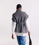 Poncho de punto color gris con cuello alto y diseño de manga corta sin sisa. Incluye un cinturón del mismo material para ajustar a la cintura y presenta una textura acanelada.