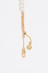 Pulsera dorada de doble cadena, una de eslabones y otra con perlas. Incluye un dije redondo con un corazón negro y logo grabado.