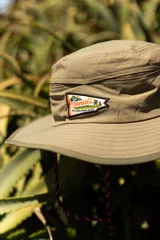 Sombrero tipo pescador color beige con ala ancha, borde reforzado, correa ajustable y parche frontal con el logo de Denali.