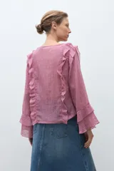 Blusa de manga larga color rosado con textura, escote redondo y volados decorativos en los hombros y a lo largo del frente.