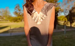 Vestido corto tejido en hilado de algodón color beige, con cuello en V y apliques de cuero en tonos dorados y marrones.