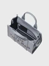 Bolso tote pequeño de cuero color negro, con doble asa corta y correa lateral. Estampado frontal con el nombre de la marca y el tipo de bolso.