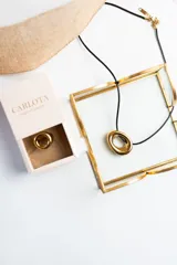 Collar con cordón negro y dije dorado con forma de doble aro entrelazado.