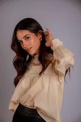 Camisa color crema con cuello alto y mangas largas con volados en los puños. Presenta detalles de crochet y broderie en el frente.