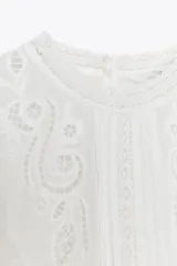 Blusa negra de algodón con cuello redondo y manga corta abullonada. Presenta bordados a tono y cierre en la espalda con abertura y botón.