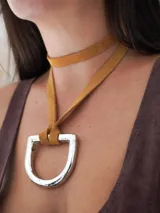 Collar con tira de cuero color suela y dije metálico dorado en forma de estribo.