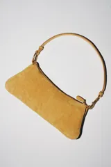 Bolso de hombro alargado color mostaza, confeccionado en piel serraje. Cuenta con tres compartimentos interiores y un bolsillo interior con cierre de cremallera. El asa de hombro tiene detalles metálicos y el cierre es mediante cremallera.