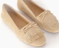 Mocasín color beige de cuero gamuzado con flecos y lazo con herrajes metálicos dorados en la capellada. Interior forrado en cuero y suela de goma flexible.
