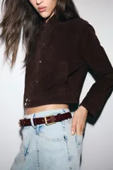 Cazadora de ante 100% piel con cuello solapa, manga larga y bolsillos delanteros de vivo. Presenta cierre frontal con cremallera oculta y botones a presión.