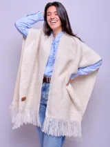 Ruana de lana merino natural sin teñir tejida de forma artesanal en telar, con flecos en el borde inferior y etiqueta de cuero en una esquina.