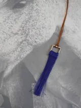 Collar con cordón de cuero marrón y dije cuadrado de metal con flecos rojos.