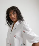 Vestido camisero midi blanco con estampado de flores rosas y celestes, manga corta abullonada, cuello camisero, abotonado al frente y falda con volantes.