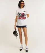 Remera blanca de algodón con cuello redondo y mangas cortas. Estampa frontal con diseño de casco de carreras, bandera a cuadros y texto "Racing Fast and Fun".