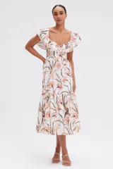 Vestido midi blanco con estampado floral en tonos naranja y marrón. Presenta escote cuadrado con volados, mangas cortas con volados y falda escalonada con volados.