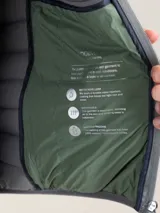 Chaleco gris acolchado para hombre, confeccionado en nylon reciclado repelente al agua, con cierre de cremallera, sisa elástica y logo engomado en el pecho.