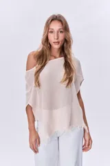 Poncho de tejido de punto color beige, con cuello amplio y terminación con flecos.