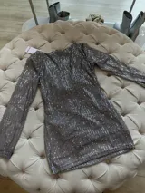 Vestido corto plateado de lentejuelas con mangas largas acampanadas y espalda descubierta que se ata con tiras.